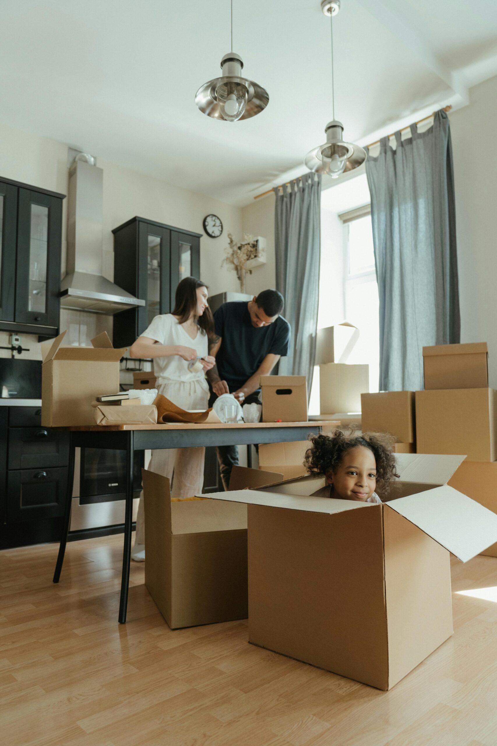 Family moving into their new home surrounded by cardboard boxes. Child plays joyfully in a box.